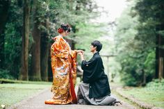 two people in kimonos sitting on the ground next to each other and touching hands