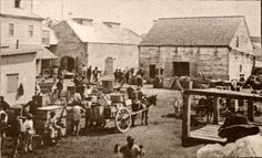 an old black and white photo shows people standing around in front of buildings with horse drawn carriages