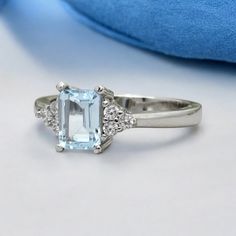 an aqua blue topazte and diamond ring sits on a white surface next to a blue pillow