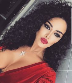 a woman with long black curly hair wearing a red top and lipstick on her lips