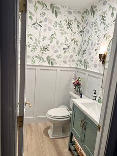 a white toilet sitting in a bathroom next to a sink and wooden floored floors