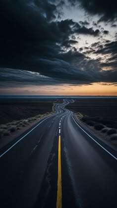 an empty highway in the middle of nowhere at night with dark clouds above it and yellow lines painted on the road