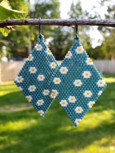 two blue and white beaded earrings hanging from a tree branch in front of green grass