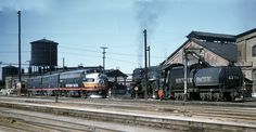 two trains are parked on the tracks in front of an old building and water tower