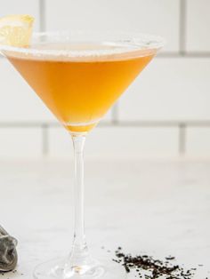 an orange cocktail in a martini glass with a lemon slice on the rim next to it