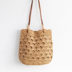 a crocheted straw bag hanging on the wall with leather handles and strap around it