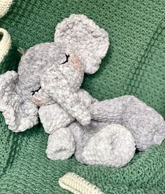 a crocheted gray teddy bear laying on top of a green blanket