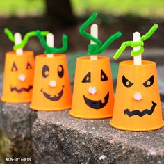 four plastic cups with faces painted on them sitting on a rock in front of a tree