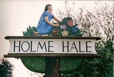 a sign that says holme hale with a woman sitting on top of it