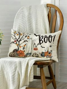 a chair with a pillow that says boo on it next to a white blanket and pumpkins