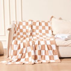 a white and brown checkered blanket sitting on top of a couch next to pillows