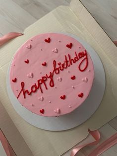 a birthday cake with pink frosting and red hearts on it, sitting in a box