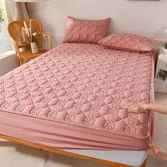 a bed with pink bedspread and pillows on it in a room next to a window