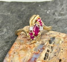 Such a delicate and pretty 14kt Gold setting in this Ruby and Diamond ring. A larger marquise shaped Ruby sets the stage, smack dab in the middle of four other round rubies and two round diamonds! The round stones nestle around the Ruby marquise in a flowing type shape with the 14kt Gold setting wrapping around them. I cleaned the ring and boy does it shine! Stones are all in very good, stable condition. The setting is also solid with beautifully graceful tendrils joining together under the stones. Perfect gift for the July birthday in your life! Size 6 1/4 US. Marked 14kt on inside of band. Weighs .2 oz. This piece hails from an estate in Colorado.  The Ruby is known as a protective stone that can bring happiness and passion into the life of the wearer. Apart from its red color, this is w Marquise Ruby Ring With Diamond Accents As Gift, July Birthday, Diamond Cocktail Rings, Me Clean, Bring Happiness, Gold Set, 14kt Gold, Birthday Gifts For Her, Cocktail Rings