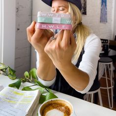 a woman sitting at a table with a cup of coffee in front of her face