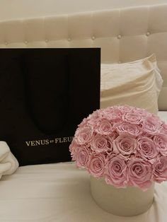 a bouquet of pink roses sitting on top of a bed next to a black box