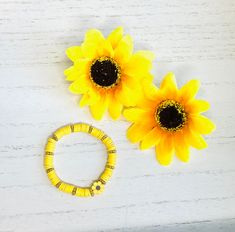 three yellow sunflowers sitting next to each other on a white wooden table with a beaded bracelet