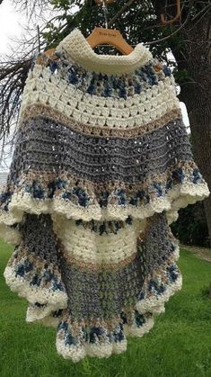 a crocheted sweater hanging from a tree in front of a house on the grass