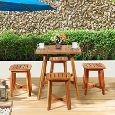 three wooden stools sit under an umbrella on a deck next to a stone wall