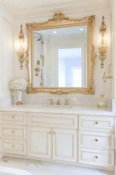 a bathroom with white cabinets and gold trimmings on the mirror above the sink