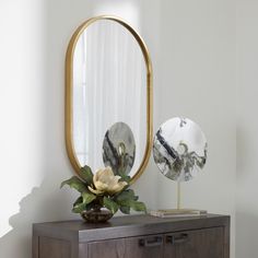 a mirror sitting on top of a dresser next to a vase with flowers in it