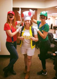 three women dressed up as mario and luigi in an office setting, posing for the camera