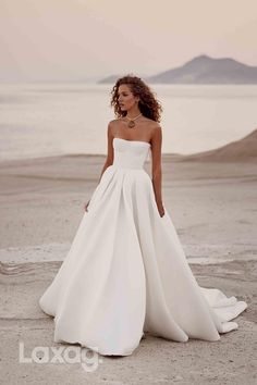 a woman in a white wedding dress standing on the beach with her back to the camera