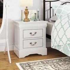 a white night stand with two drawers and a gold lamp on the nightstand next to it