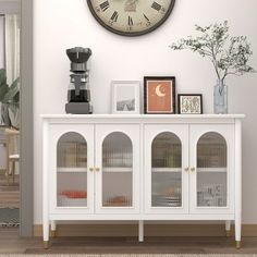 there is a clock on the wall above a white cabinet with glass doors and drawers