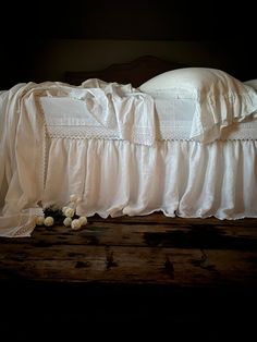 a bed with white ruffled bedspread and flowers on the floor next to it