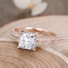 an engagement ring with a princess cut diamond in the center on top of a piece of wood