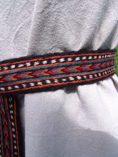 a close up of a person wearing a white shirt and black belt with colorful braiding on it