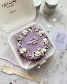 a purple cake sitting in a white box on top of a table next to other items