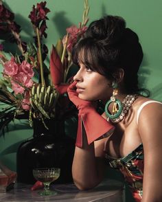 a woman sitting at a table with flowers in front of her and wearing red gloves