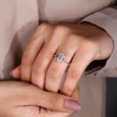 a woman's hand holding an engagement ring with a diamond in the middle, on top of her finger