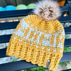 a knitted hat with a pom - pom sits on a park bench