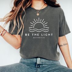 Shine your light and share your faith with our "Be The Light" t-shirt, inspired by Matthew 5:14. This minimalist and elegant design is perfect for those who want to wear their faith proudly. Whether you're attending a church service, a community event, or simply want to carry a message of hope and light in your daily life, this shirt is a meaningful addition to your wardrobe. ⭐✨ K E Y * D E T A I L S ✨ 🌈 Colors may vary slightly due to fabric and screen differences, giving each piece a unique t Be The Light Shirt, Bible Verse Gifts, Church Shirt, Faith Tees, Be The Light, Shine Your Light, Jesus Shirt, Religious Shirt, Church Service