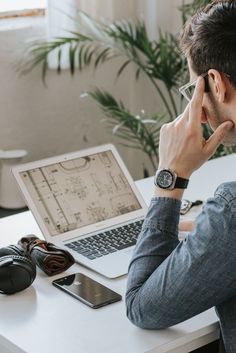 a man sitting in front of a laptop computer while holding his head to his ear