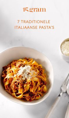 a white bowl filled with pasta and sauce on top of a table next to utensils