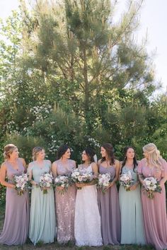 a group of women standing next to each other in front of a tree holding bouquets