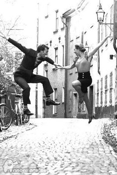 two people jumping in the air on a cobblestone street