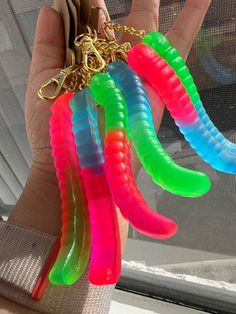 a person holding up several different colored plastic objects in front of a glass window with a gold keychain hanging from it