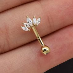 a tiny gold nose piercing with three leaves on it's end, in the palm of someone's hand