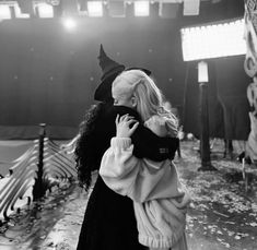 black and white photograph of woman in witch costume holding child on her back while walking through an empty stadium