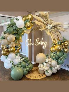 a balloon arch decorated with gold, white and green balloons for a baby's first birthday