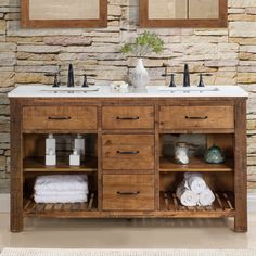 a bathroom vanity with two sinks and towels on the shelf next to it, against a stone wall