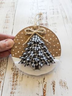 a hand holding a wooden ornament with a small christmas tree on it's side