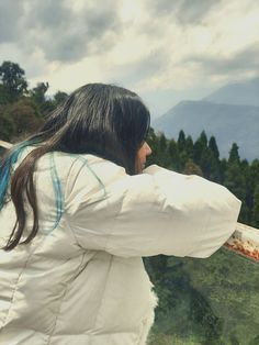 a woman is looking out at the mountains and trees from an observation platform on a cloudy day