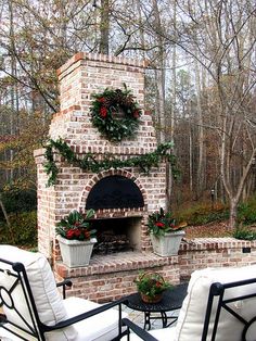 an outdoor fireplace with potted plants and wreaths on the mantle is surrounded by chairs