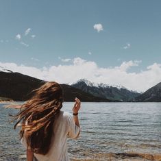 a woman standing on top of a rocky beach next to a large body of water